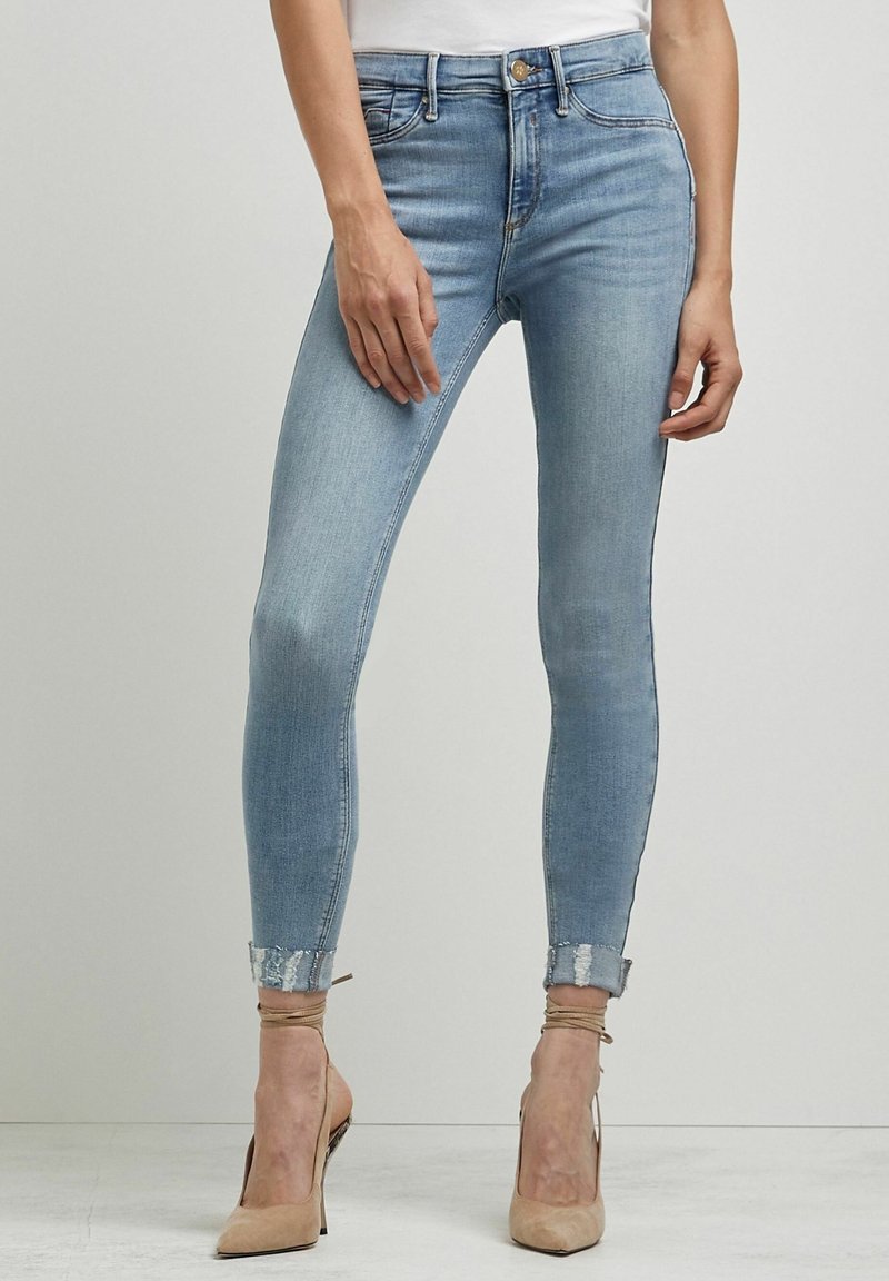 Jeans ajustados de denim azul claro con un acabado desgastado, que cuentan con una cintura alta, puños enrollados y sutiles detalles de costura.
