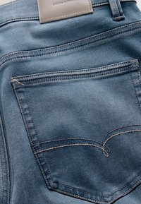 Dunkelblaue Jeans aus Denim mit einer Gesäßtasche, die kontrastierende Nähte und ein Lederetikett am Taillenbund aufweist. Glatter, strukturierter Stoff.
