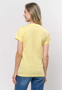 Kollane lühikeste varrukatega T-särk pehmest puuvillakangast, millel on ümara kaelusega lõige ja mugav lõige, kombineeritud siniste teksadega.