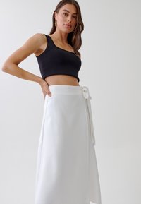 Top court noir sans manches et jupe enroulée blanche avec un nœud sur le côté, présentant une texture de tissu lisse et une silhouette fluide.