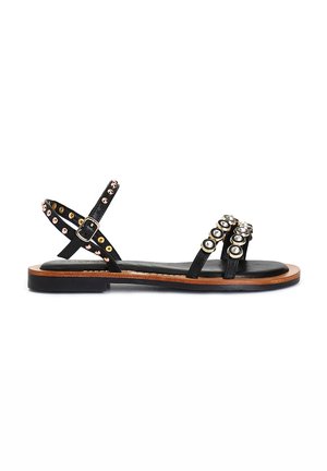 Sandali in pelle nera con multiple cinghie, accentuati da borchie metalliche rotonde in oro e argento, e una suola in legno piatta.