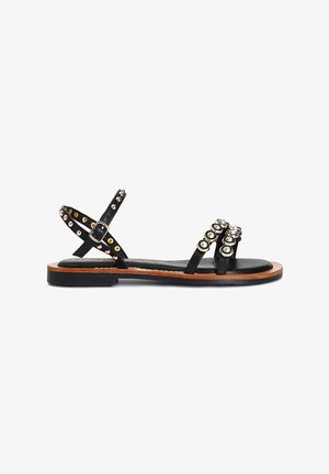 Schwarze Leder-Sandalen mit mehreren Riemen, akzentuiert von runden, metallischen Nieten in Gold und Silber, sowie einer flachen Holzsohle.