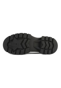 Semelle d'une botte noire avec des crampons profonds, un motif en forme d'étoile près du talon et des rainures en zigzag pour la traction et la durabilité.