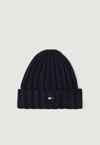 Marineblå strikket lue med ribbet tekstur, som har en liten, rektangulær logo i hvitt, rødt og blått på den brettede mansjetten.