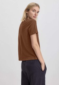 T-shirt corto marrone a maniche corte con vestibilità comoda, realizzato in tessuto morbido, abbinato a pantaloni blu scuro con tasche laterali e un design semplice.