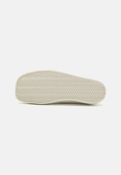 Gummiskosula i off-white, med ett vågigt mönster. Slät yta med rundade kanter och en lätt krökning vid tån.