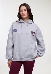 Felpa grigia con cappuccio, tasca frontale e coulisse. Presenta una toppa blu con la scritta "COLORADO" e il numero "80" in bordeaux sul davanti. Tessuto morbido.