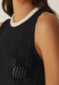 Haut noir sans manches avec un motif tricoté texturé et une encolure blanche tressée. Vue en gros plan des détails de l'épaule et de l'encolure.