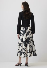 Black long-sleeve top paired with a flowy, knee-length skirt featuring a bold black and white abstract pattern. Black heeled sandals complete the look.