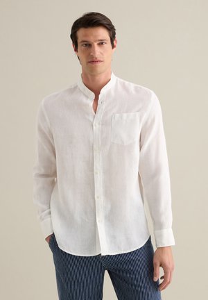 White linen shirt with a band collar, button front, and a single chest pocket, worn with navy striped trousers. Smooth, lightweight texture.