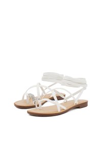 Sandali bianchi con fasce, dotati di suola piatta, caratterizzati da un accento decorativo in argento e fasce morbide e flessibili realizzate in materiale sintetico.