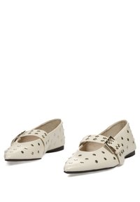 Zapatos de punta en charol crema, con acentos de tachuelas, una cinta cruzada con un hebilla plateada y un tacón bajo.