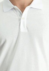 Polo bianco con colletto classico, placca con due bottoni, tessuto testurizzato e una leggera lucentezza. Vestibilità slim, maniche corte.