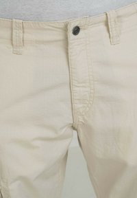 Beige katoenen blend broek met een fijn geruit patroon. Kenmerkt zich door een metalen knoopsluiting en zijdetails bij de zakken.