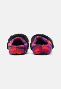 Une paire de chaussons en peluche avec un motif écossais noir, violet et orange, vue de l'arrière sur un fond blanc.