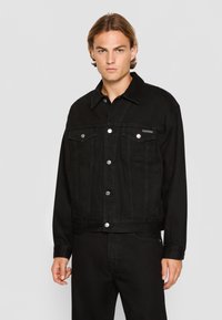 Black denim jacket featuring button-up front, two chest pockets, and a point collar. Smooth texture with subtle stitching details.