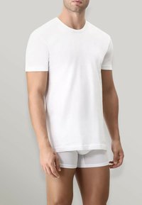 T-shirt bianco in cotone con maniche corte, scollo rotondo e vestibilità rilassata, abbinato a boxer bianchi semi-trasparenti.