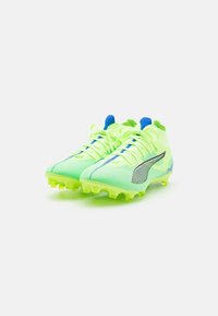 Scarpe da football verde lime con materiale in rete, dettagli blu, marchi neri e argentati, e suola texture per aderenza.