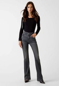 Jean évasé taille haute en denim gris foncé. Comprend cinq poches, un léger délavage et une fermeture classique à boutons. Orné d'un haut noir.