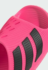 Sandale mule rose vif avec surface texturée et trois bandes diagonales noires sur le dessus.