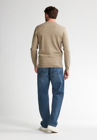 Khakifarbener, strukturierter Strickpullover mit horizontalen Streifen, kombiniert mit hellblauen, lässig geschnittenen Jeans und weißen Sneakers. Von hinten betrachtet.