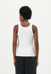 Hvit, ribbet tanktop med tettsittende design, rund hals og brede stropper, kombinert med svarte bukser med blomstermønster.