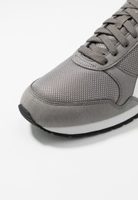 Graue Sneaker mit Obermaterial aus Mesh und Wildleder, runder Zehenpartie und Schnürverschluss. Schwarze Gummisohle mit weißen Mittelsohlenelementen.