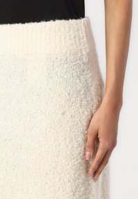 Knit cream skirt with a ribbed waistband, textured fabric, and close-fitting design. The texture appears soft and fuzzy.