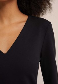 Czarny top z dekoltem w serek i długimi rękawami, wykonany z gładkiego, lekko teksturowanego materiału. Charakteryzuje się głębokim dekoltem i dopasowanym krojem.