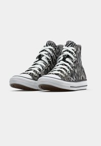 Adidași negri și gri, tip pantof înalt, cu imprimeu animal, șireturi albe și vârf din cauciuc alb. Au o talpă texturată pentru aderență.