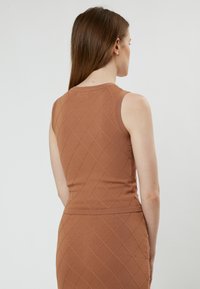 Top senza maniche lavorato a maglia marrone con un motivo a diamante, caratterizzato da un collo rotondo e una silhouette aderente. Il tessuto appare liscio e con texture.