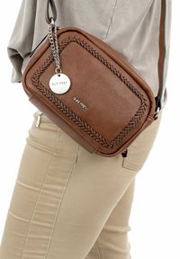 Borsa a tracolla in pelle marrone con dettagli intrecciati, forma rettangolare, accessori in argento e etichetta con logo. Indossata di lato a una persona.