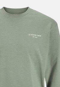 Hellgrünes Langarm-T-Shirt aus weichem Material mit Rundhalsausschnitt und weißem Text: "JJ DENIM CREW Est. 1990" auf der Brust.