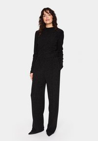 Svart jumpsuit med långa ärmar, något lös passform och texturerad tygkvalitet. Har en hög krage och vida byxor.