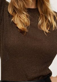Haut en tricot côtelé marron avec un col rond, présentant une texture scintillante et une silhouette ajustée. Met en valeur la forme du corps.
