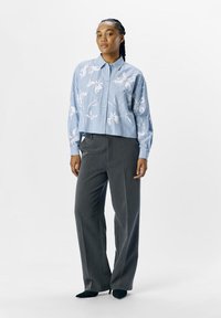 Camicia a righe blu e bianca con bottoni e motivo floreale; abbinata a pantaloni grigi a gamba larga; tessuto morbido, vestibilità rilassata.