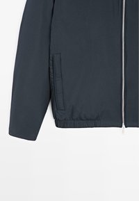 Ciemnogranatowa kurtka o gładkiej fakturze, wyposażona w srebrny zamek błyskawiczny, elastyczny pas i boczne kieszenie. Prosty, nowoczesny design.