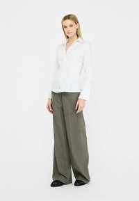 Weißes Hemd mit langen Ärmeln, kombiniert mit beigefarbenen und grünen gemusterten Schlaghosen und schwarzen Schuhen. Einfaches und strukturiertes Design.