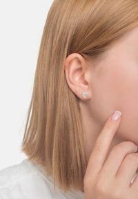 Hjärtförformade silverörhängen med en färgglad steninläggning, med en slät yta och en polerad look, som bärs på en models öra.