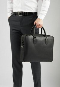 Sort læderbriefcase med struktureret overflade, dobbelte top-håndtag og sølvfarvede detaljer. Lynlåslukning og synlig sidelomme.