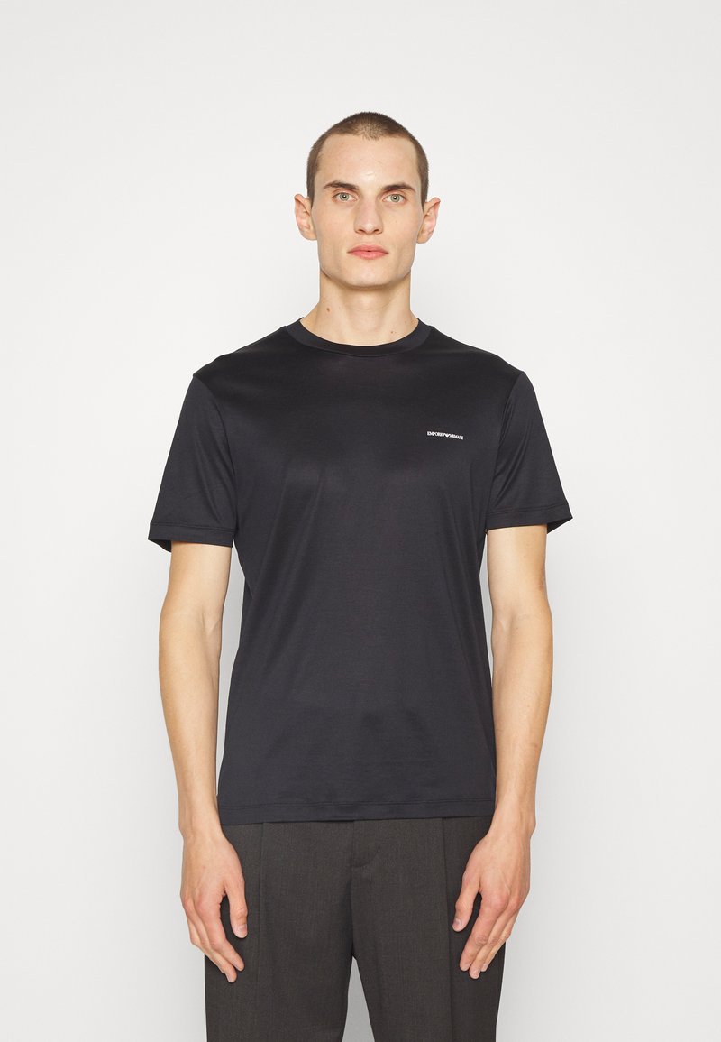 Juoda crew neck marškinėliai, pagaminti iš minkštos medžiagos, su trumpomis rankovėmis ir mažuoju logotipu ant krūtinės. Paprastas ir prigludęs dizainas.