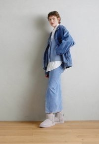 Lyseblå denimjakke over en lyseblå strikkegenser, hvit skjorte og lyseblå utvidede jeans, komplementert med grå ankelstøvler.