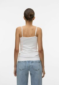Canotta bianca, aderente, con spalline sottili, tessuto liscio e design semplice, abbinata a jeans azzurri larghi con tasche posteriori.