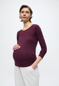 Μπλούζα εγκυμοσύνης σε σκούρο μωβ, με μακριά μανίκια και λαιμόκοψη με στρογγυλεμένο V, με ρεβέρ στα πλάγια για εφαρμοστή εμφάνιση. Άνετο ύφασμα από βαμβακερό μείγμα.