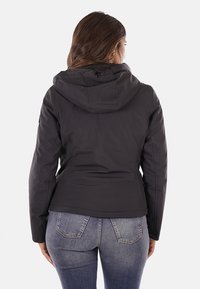 Giacca nera con cappuccio, dalla texture liscia, design aderente e polsini elasticizzati. La vista posteriore mostra le cuciture e una lunghezza leggermente accorciata.