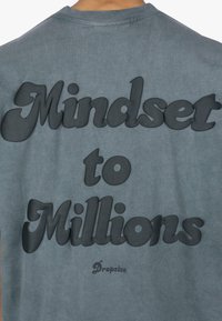 Sivá bavlnená tričko s veľkým, embosovaným čiernym textom "Mindset to Millions" na zadnej strane, pod ním v menšom písme značka "Dropsize".