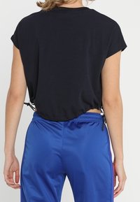 Černé zkrácené tričko s krátkými rukávy a stahovací šňůrkou na spodním okraji, v kombinaci se lesklými modrými tepláky s elastickým pasem a bočními pruhy.