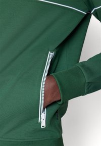 Felpa verde con finitura testurizzata, dotata di una tasca con zip con dettagli bianchi e polsini, e un sottile contrasto di colore nel design.