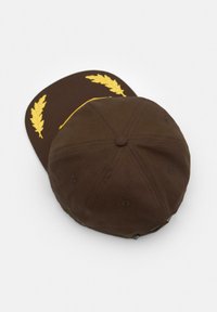 Brączowa czapka z zakrzywionym daszkiem, z żółtym haftem liści wawrzynu na przedzie. Wykonana z tkaniny, ma strukturalny design składający się z sześciu paneli.