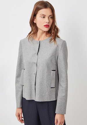 Chaqueta gris con textura, cuello redondo, cierre de botones y dos bolsillos frontales con ribete negro. Mangas largas, ajuste entallado.